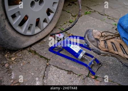 Mann, der eine Fußpumpe mit manuellem Luftdruck betreibt, um einen platten, durchbrochenen Autoreifen aufzupumpen Stockfoto