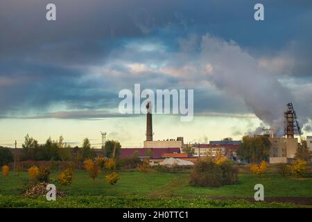 Rauch, der bei Sonnenuntergang aus industriellen Rauchgesteinen in einer Fabrik oder Anlage aufwabt und die Luft und die natürliche Umwelt durch Kohlenstoffemissionen und -emissionen verschmutzt Stockfoto