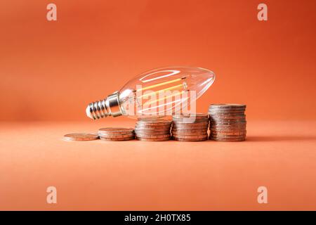 led-Glühbirne auf Münzen in Form einer aufsteigenden Grafik, die die steigenden Stromkosten symbolisiert. Stockfoto
