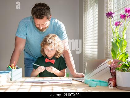 Bärtiger Vater schreibt Schulaufgaben mit seinem Sohn im Klassenzimmer, moderne Bildung Stockfoto