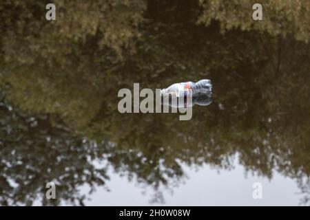 Weggeworfene alkoholfreie Getränkeflaschen aus Kunststoff, die in einem Kanal schwimmen und die Plastikverschmutzung erhöhen, die auf dem Planeten dringende Umweltprobleme verursacht Stockfoto