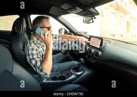 Mann fährt ein Auto und nutzt Infotainment. Der Fahrer liest Nachrichten und telefoniert während der Fahrt. Gefährliches Verhalten, Unfallrisiko. Gefahr, trans Stockfoto