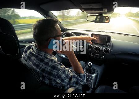 Mann fährt ein Auto und nutzt Infotainment. Der Fahrer liest Nachrichten und telefoniert während der Fahrt. Gefährliches Verhalten, Unfallrisiko. Gefahr, trans Stockfoto