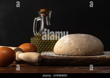 Frischer roher Teig für Brot oder Pizza mit Eiern auf einem dunklen Holztisch. Stockfoto