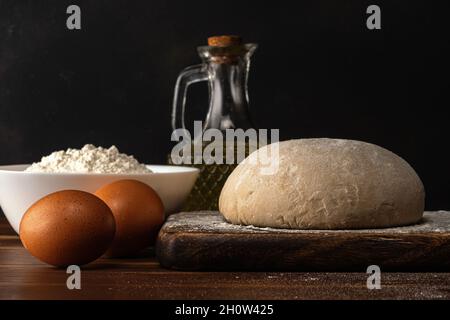 Frischer roher Teig für Brot oder Pizza mit Eiern auf einem dunklen Holztisch. Stockfoto