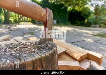 Altes Werkzeug aus Stahl mit Spuren von roter Farbe in Log aufgespießt. Beil-Werkzeug zum Spalten von Baumstümpfen und Zerkleinern von Baumstämmen in einem Garten. Stockfoto