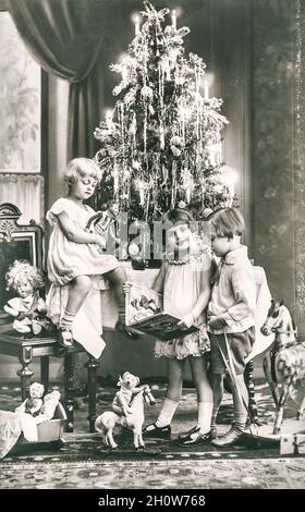 Weihnachtsbaum, Kinder, Geschenke und Vintage-Spielzeug. Vintage-Postkartenbild Stockfoto