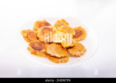 Haufen gebratener und zerschmetterter Bananen auf weißem Hintergrund. Patacones, Tostones, Chips, reifer Kochbananen. Auf einem weißen Teller. Stockfoto