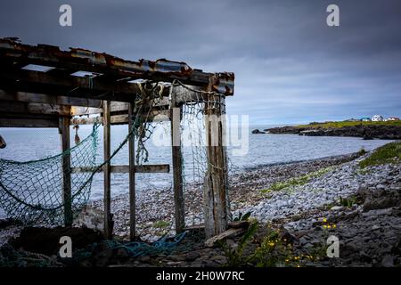 Verlassene Fischernetzschuppen an einem grauen, steinigen Strand. Wolkiger Himmel. Stockfoto