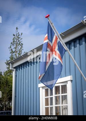 Hafnarfjordur, Island - 17. Juli 2021: Isländische Flagge auf einem blauen Gebäude des Hafnarfjordur Museums. Sonniger Tag, blauer Himmel. Stockfoto