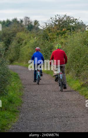 Ein älteres Paar mittleren Alters, das auf der Insel wight Fahrräder entlang einer Landstraße fährt, Radfahrer auf einem Landweg oder Radweg, die Fahrräder fahren. Stockfoto