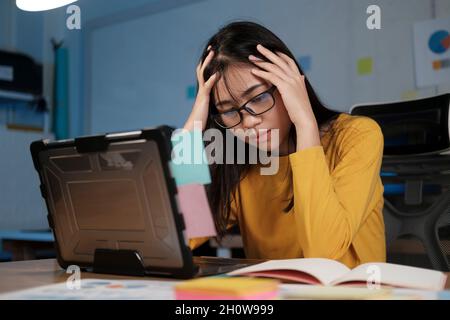 Gestresste, erschöpfte Frau, die am Schreibtisch sitzt und Überstunden macht, ist mit Arbeit überladen. Stockfoto