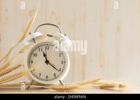 Kleiner weißer Vintage-Wecker mit Ähren aus Weizen auf weißem Holzhintergrund mit Kopierfläche Stockfoto