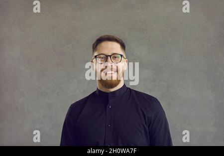 Porträt eines lächelnden hübschen und selbstbewussten kaukasischen jungen Mannes auf grauem Hintergrund. Stockfoto