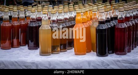 Reihen von bunten Flaschen mit hausgemachter Alkoholtinktur, die draußen auf dem Tisch stehen. Stockfoto