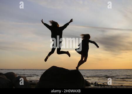 Silhouetten von springenden Kindern auf dem Hintergrund des Sonnenuntergangs. Stockfoto