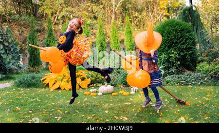 Kleine Hexe fliegt an Halloween auf einem Besenstiel.zwei Mädchen in einem Hexenkostüm lernen, auf einem Besen zu fliegen, der in die Luft springt. Kinder im Karneval Stockfoto