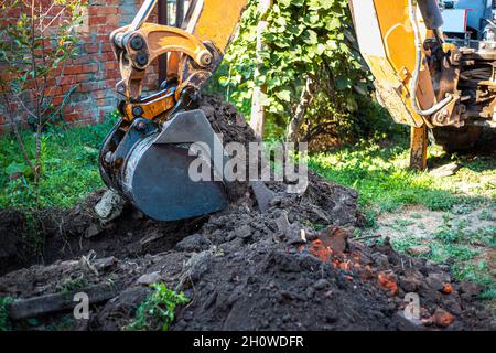 Der Bagger gräbt den Boden mit einem großen Eimer auf dem Grundstück, um ein Wasserversorgungssystem zu legen. Stockfoto