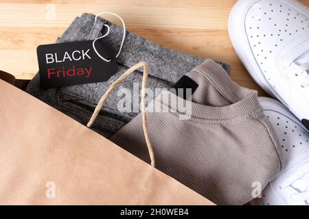 Stilvolle Herrenbekleidung in einer Papiertasche mit Schuhen mit einem schwarzen freitagsschild auf einem Holztisch. Stockfoto