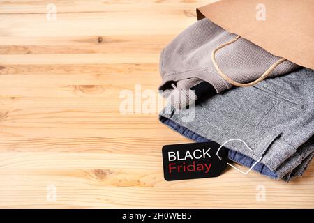 Neue Herrenbekleidung in einer Papiertüte mit einem schwarzen freitagsetikett auf einem Holztisch mit Meté für Text. Stockfoto