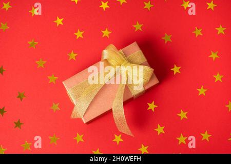 Helles Geschenk in goldener Verpackung und einer Schale mit goldenen Bändern auf farbigem Hintergrund mit glänzenden Sternen. Stockfoto