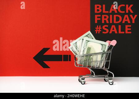 Black Friday Shopping-Tag. Trolley mit Geld auf farbigem Hintergrund und einer Inschrift. Stockfoto