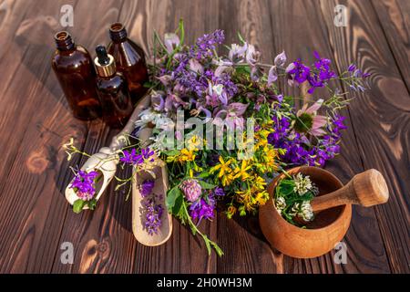 Sommer Heilkräuter - Johanniskraut, Kamille, Kleeblatt in der Nähe von Holzmörtel. Flaschen für Kosmetika aus natürlichen Kräutern. Stockfoto