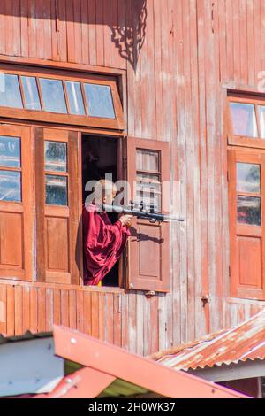 INLE, MYANMAR - 28. NOVEMBER 2016: Buddhistischer Novizenjunge mit einem BB-Gewehr in einem Kloster am Inle-See, Myanmar Stockfoto