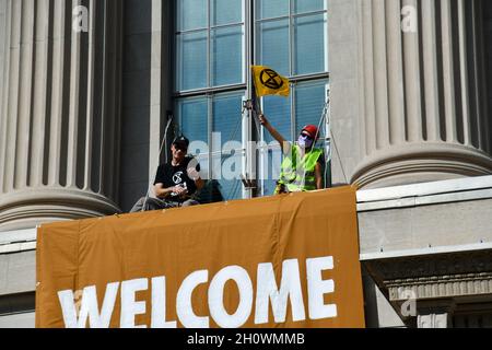 Washington, USA. Oktober 2021. Ein Umweltaktivist der Gruppe Extinction Rebellion schwenkt eine Flagge vor einem Fenster im zweiten Stock der US-Handelskammer, als Protest gegen die Haltung der Organisation zum Klimawandel in Washington, DC, am 14. Oktober 2021. Die Aktivisten gingen über eine Leiter in den zweiten Stock, um zwei große Transparente zu entrollen und wurden bei ihrem Abstieg von der Polizei verhört und freigelassen. (Foto: Matthew Rodier/Sipa USA) Quelle: SIPA USA/Alamy Live News Stockfoto