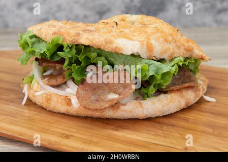 Frisch gebackenes Panuozzo Pizza Sandwich mit allen Belägen im Inneren auf einer Holzplatte serviert. Stockfoto