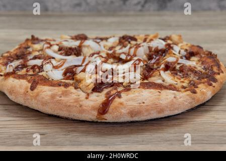 Frisch gebackene BBQ-Hähnchenpizza mit gehackten Fleischstücken, serviert auf einer Holzplatte. Stockfoto