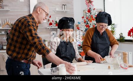 Enkelin bereitet Lebkuchen Dessert Herstellung traditioneller hausgemachter Teig mit Nudelholz in Weihnachten dekoriert kulinarische Küche. Glückliche Familie genießen Kochen während der weihnachtsferien Stockfoto