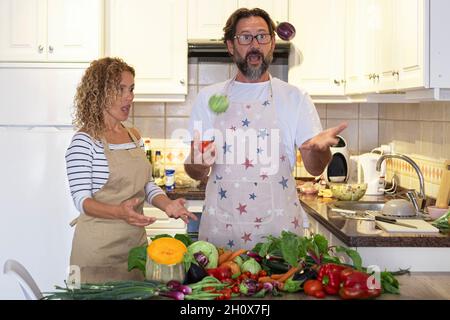 Reife junge Erwachsene Mann und Frau spielen und haben Spaß in der Küche während der Mittagsvorbereitung mit frischem Gemüse. Glückliche Paare genießen die Zeit dazu Stockfoto