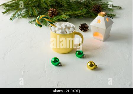 Schmutzige Weihnachtsschokolade oder Kakao in einem gelben Keramikbecher mit Joghurt und Karamell auf weißem Grund mit Fichtenzweigen und einer Kerze Stockfoto