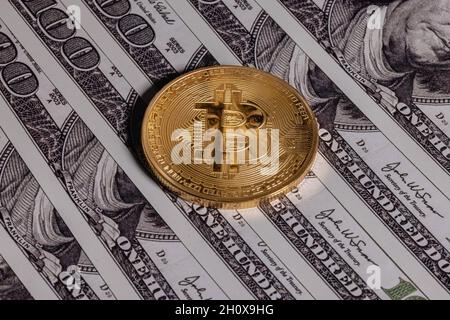 Goldbitcoin auf 100-Dollar-Scheinen. Die Münze spiegelt die Augen von Benjamin Franklin wider. Stockfoto