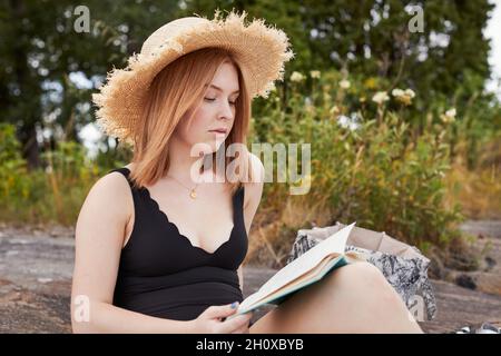 Frau trägt Strohhut und liest Buch Stockfoto