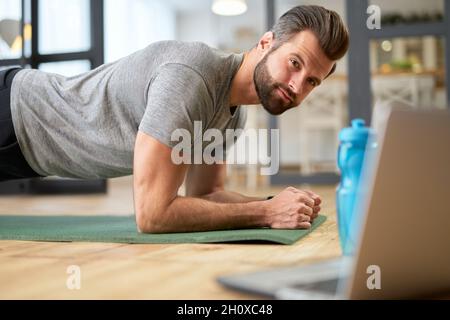 Hübscher junger Mann, der zu Hause ein Notebook benutzt und eine Planke macht Stockfoto