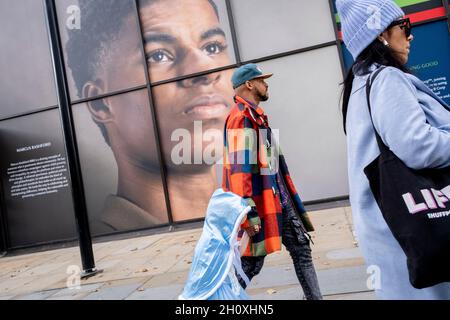 Ein Kind und ein Erwachsener gehen unter der großen Plakatwand, ein Porträt des englischen Fußballspielers Marcus Rashford, außerhalb der Strand-Filiale der Coutts Bank, am 14. Oktober 2021 in Westminster, London, England. Marcus Rashford wurde kürzlich von der University of Manchester mit einem Ehrendoktortitel in Anerkennung seiner politischen Kampagne für die benachteiligten (insbesondere Schulmahlzeiten) und seine Philanthropie ausgezeichnet. Er spielt derzeit für Manchester United und ist in der englischen Nationalmannschaft. Er wurde auch Opfer von rassischem Missbrauch im Internet. Stockfoto