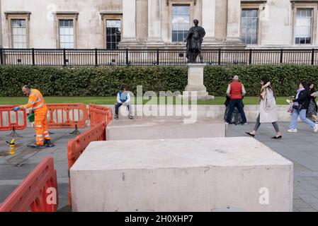 Ein Bauunternehmer reinigt am 14. Oktober 2021 in Westminster, London, Pflastersteine neben einer zeigenden Statue von König James II. (Als römischer Kaiser) auf dem Trafalgar Square. England. Stockfoto