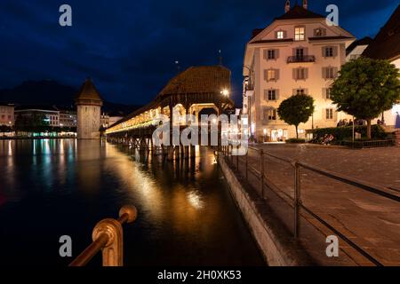 Kapellbrücke, mittelalterliche Brücke in Luzern bei Nacht. Die Brücke ist beleuchtet, die Lichter werden im See reflektiert. Beeindruckende Aussicht auf die Stadt Stockfoto