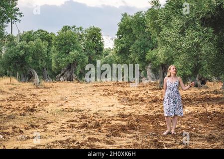 Blonde Haare Mädchen zu Fuß in einem schönen säkularen Olivenbäumen landwirtschaftlichen Feld ähnlich einer Skulptur im Herbst Stockfoto