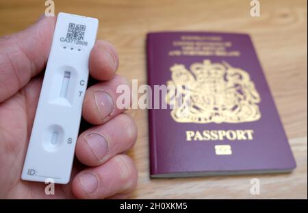 Aktenfoto vom 07/05/21 einer Person mit einem negativen lateralen Flow-Covid-19-Test vor einem Pass für das Vereinigte Königreich Großbritannien und Nordirland. Ab Oktober 24 werden neue Regeln in Kraft treten, rechtzeitig für Familien, die aus den Halbzeitferien zurückkehren, so dass Reisende, die nach England kommen, billigere laterale Durchflusstests statt PCR-Tests durchführen können. Reisende, die zu Hause einen Test machen, müssen ein Foto ihrer Test- und Buchungsreferenz machen und dieses an den privaten Testanbieter senden, um die Ergebnisse zu überprüfen. Verkehrsminister Grant Shapps sagte, die Änderung der Politik für die Post- Stockfoto