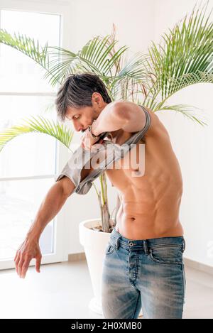 Fit getönten fünfzig Jahre alten Mann zeigt seine Bauchmuskeln, wie er auf ein Hemd in einem High-Key-Fitnessstudio in einem Gesundheits-und Fitness-oder aktiven Lebensstil Konzept Stockfoto