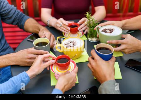 Von oben von Ernte unkenntlich Freunde sitzen an runden schwarzen Tisch und hält Tassen Kaffee und Cappuccino, während Zeit zusammen im Café zu verbringen Stockfoto