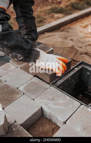 Die Technologie der Verlegung von Naturstein aus Pflasterplatten - die Arbeit eines Maurerlayers, um den Boden außerhalb zu installieren Stockfoto