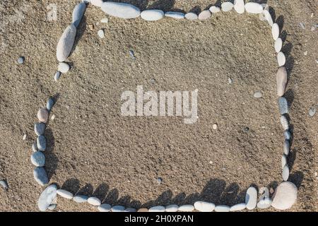 Rechteckiger horizontaler Rahmen aus Strandkieseln auf dem Sand - Hintergrund und Mockup Stockfoto