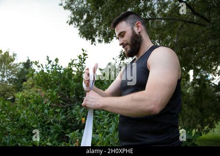 Der junge bärtige Kaukasienboxer legt Bandagen an seine Hände, um Boxen zu üben Stockfoto