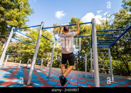 Ein Mann, der an einer horizontalen Bar in einem Park Übungen macht. Outdoor-Sport. Stockfoto