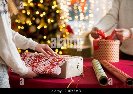 Mann und Frau bereiten sich auf Weihnachten vor. Pairle in warme Pullover Geschenkverpackung. Geschmückter Weihnachtsbaum, Schachteln mit Geschenken, buntes Geschenkpapier Stockfoto