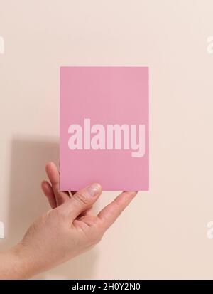 Weibliche Hand mit leerem rosa Papier auf beigem Hintergrund. Kopieren Bild oder Text einfügen, Nahaufnahme Stockfoto